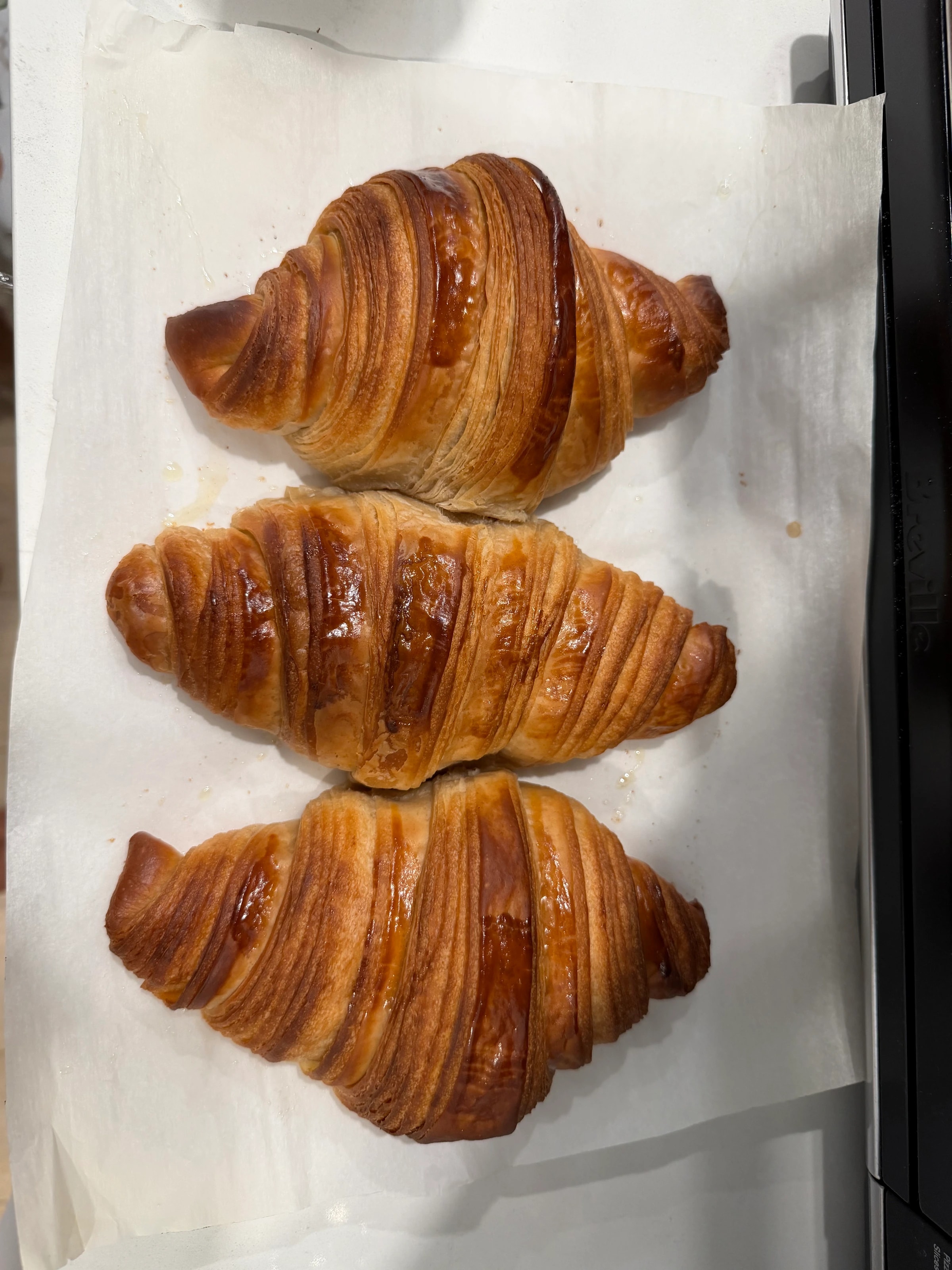 Three home-laminated croissants on parchment paper, overhead view.